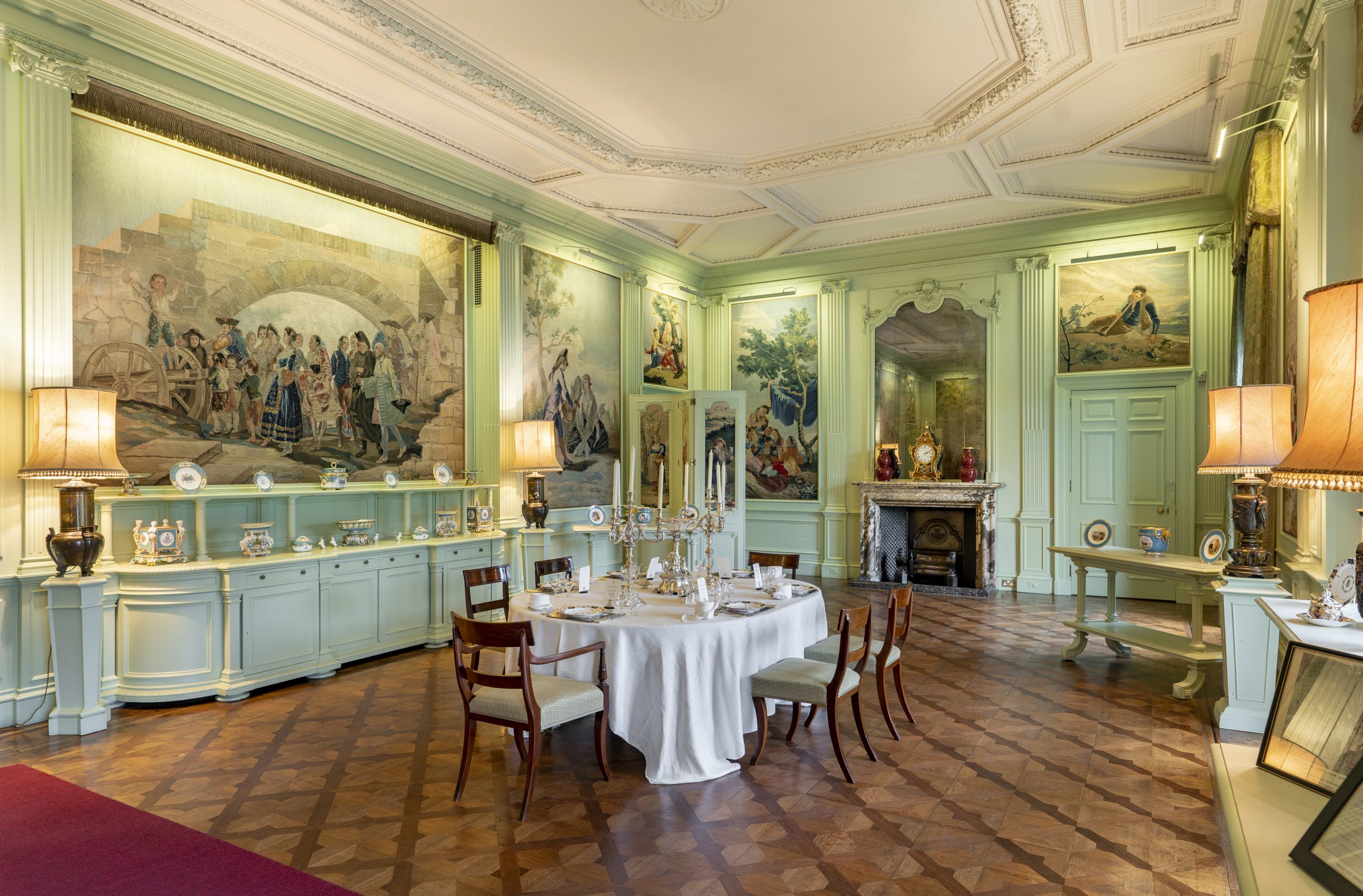 A green dining room with italian tapestries on the wall with a table set for dinner in the centre