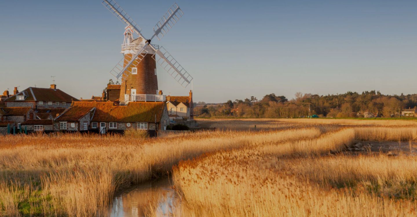 An image of a windmill with meandering river in front with grassy fields