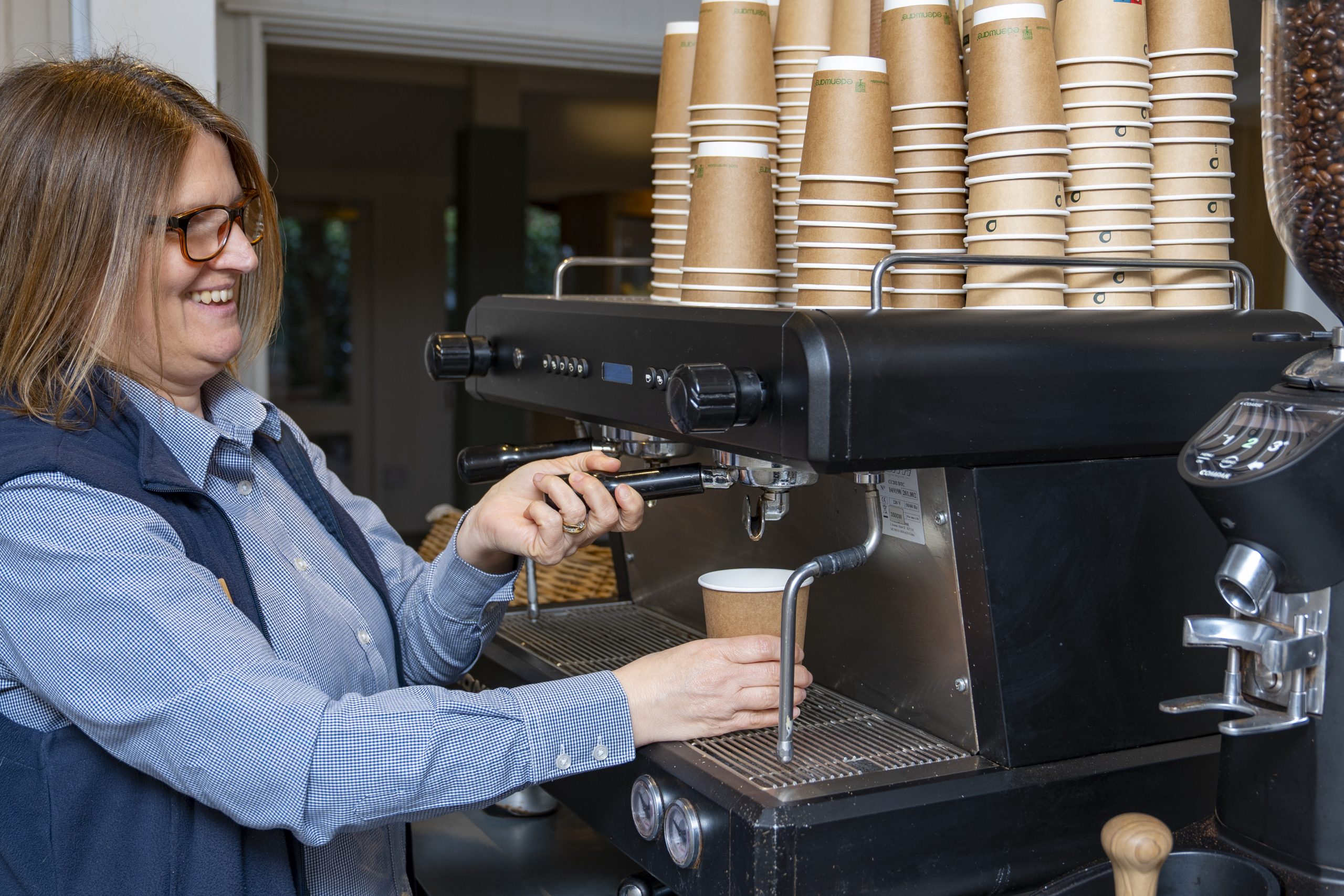 An image of a coffee machine with lots of takeaway cup and a woman making coffee